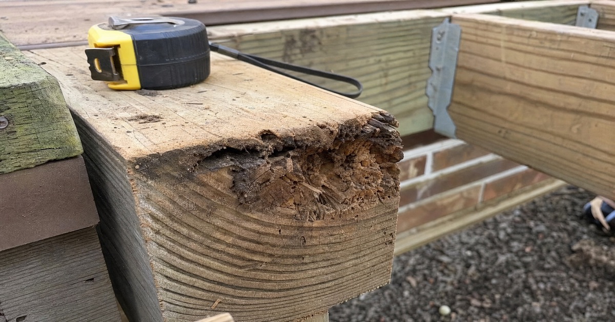 Wood deck joist with visible rot damage near the end grain, a tape measure resting nearby