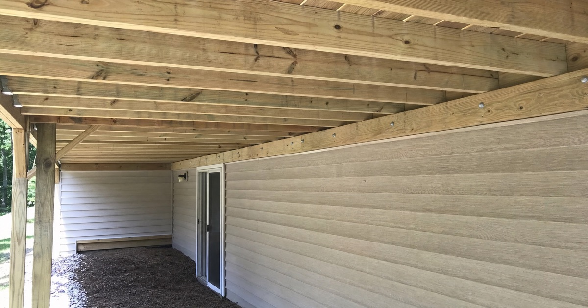 Underside of a wood backyard deck showing horizontal support joists and a ledger board